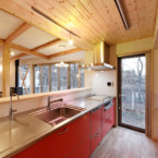 窓外に四季を映すキッチンスペース。背面にウォークスルーの収納エリアも 赤のキッチンと黒の薪ストーブがアクセント