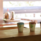 リビングより丸太のカウンター越しにダイニングキッチンを眺める 丸太のカウンターに並んだ陶器のカップ